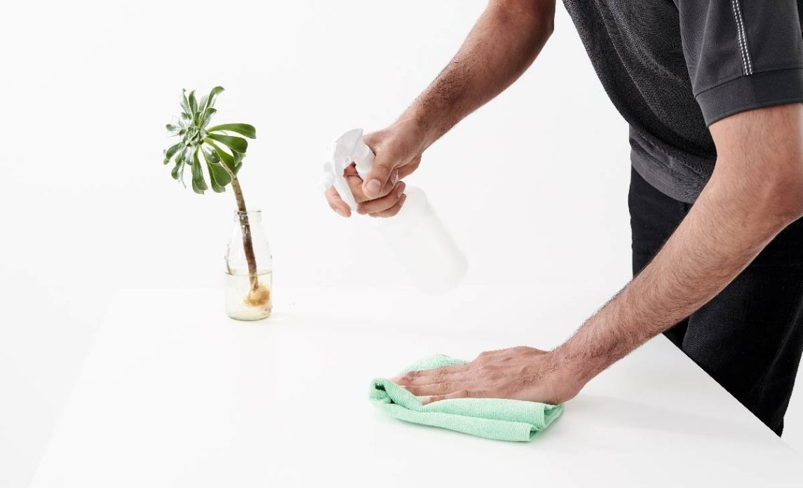 An image showing a person using a microfiber cloth to wipe down their desk, demonstrating how to clean and organize your home office