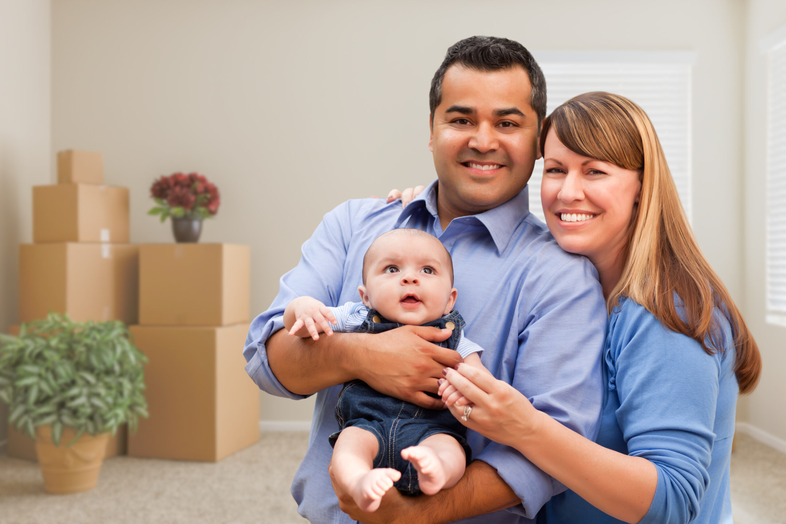 Happy Mixed Race Family with Baby in Room with Packed Moving Boxes.